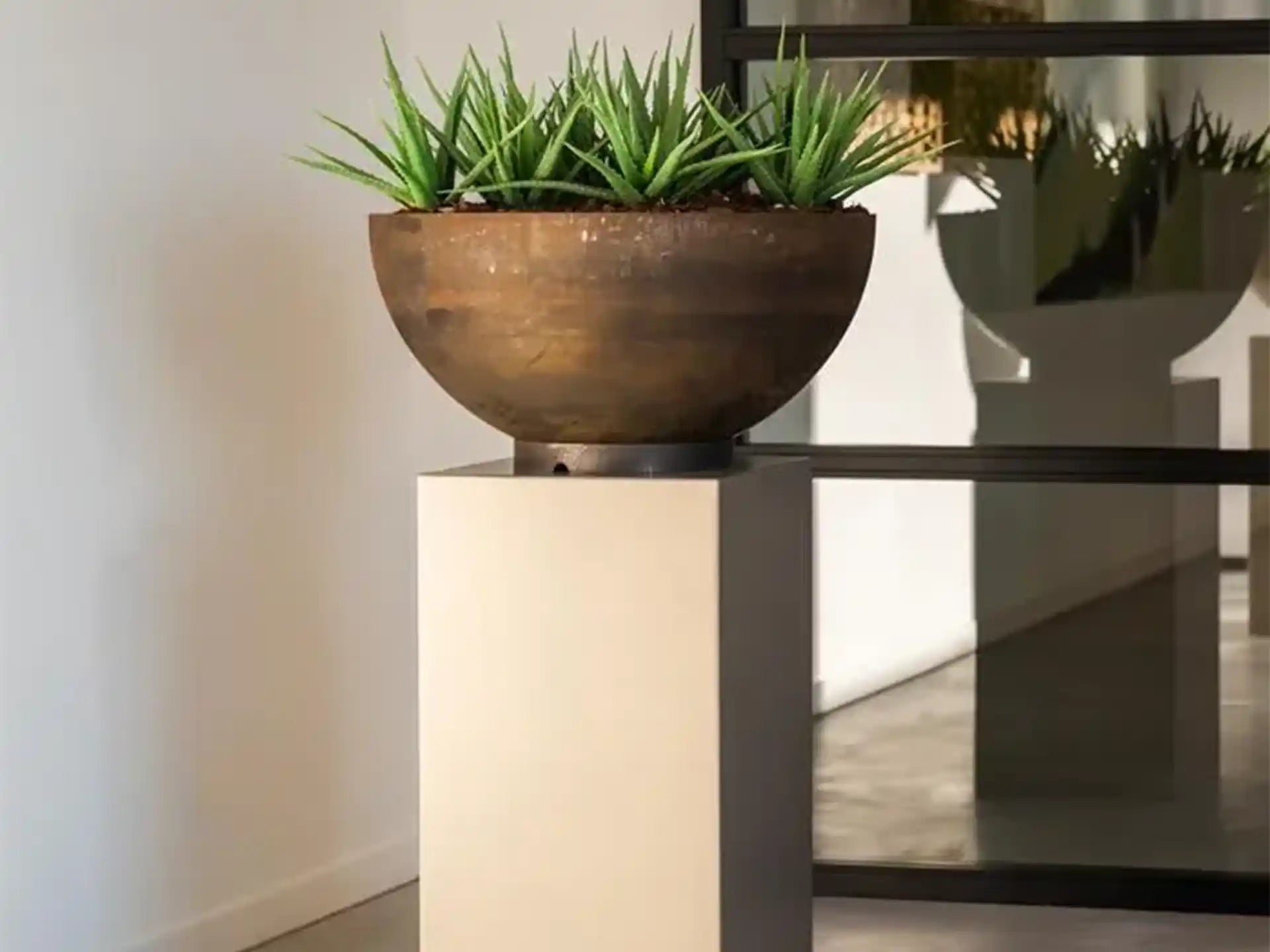 Bocca Adezz Cortenstaal Plantenbak Rond met bodem, beplant met groene agave-achtige planten in een moderne binnenruimte.