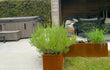 Tuin met twee cortenstalen plantenbakken van Adeqo, beplant met lavendel, siergras en witte bloemen, naast een terras met jacuzzi en zithoek.