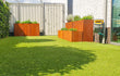 Moderne tuin met kunstgras en meerdere cortenstalen plantenbakken van Adeqo, beplant met groene planten en kruiden, geplaatst langs een witte schutting.