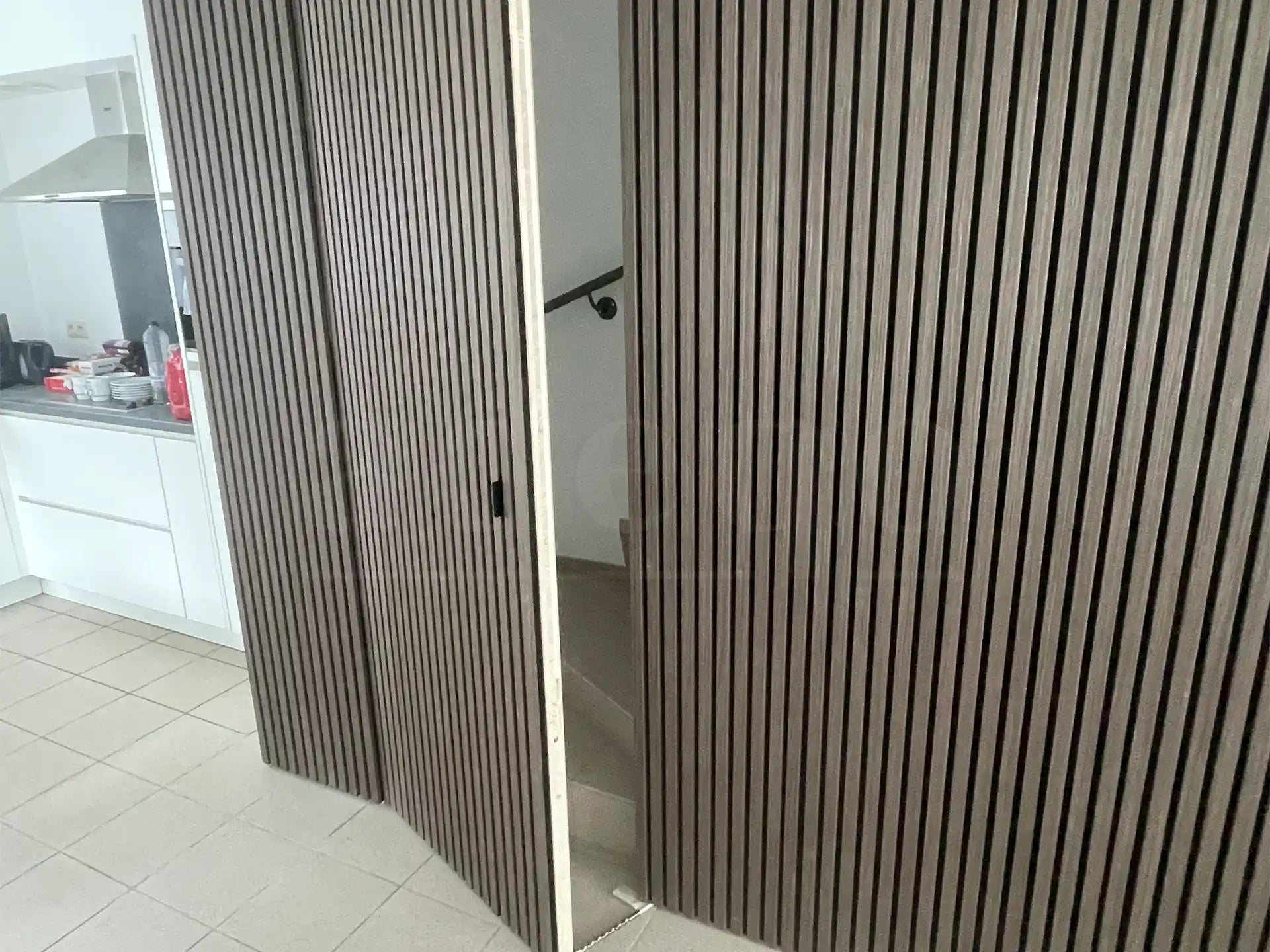 Verborgen deur naar trapopgang, bekleed met Adeqo akoestische wandpanelen in Donker Walnoot, geïntegreerd in de wand naast de keuken.
