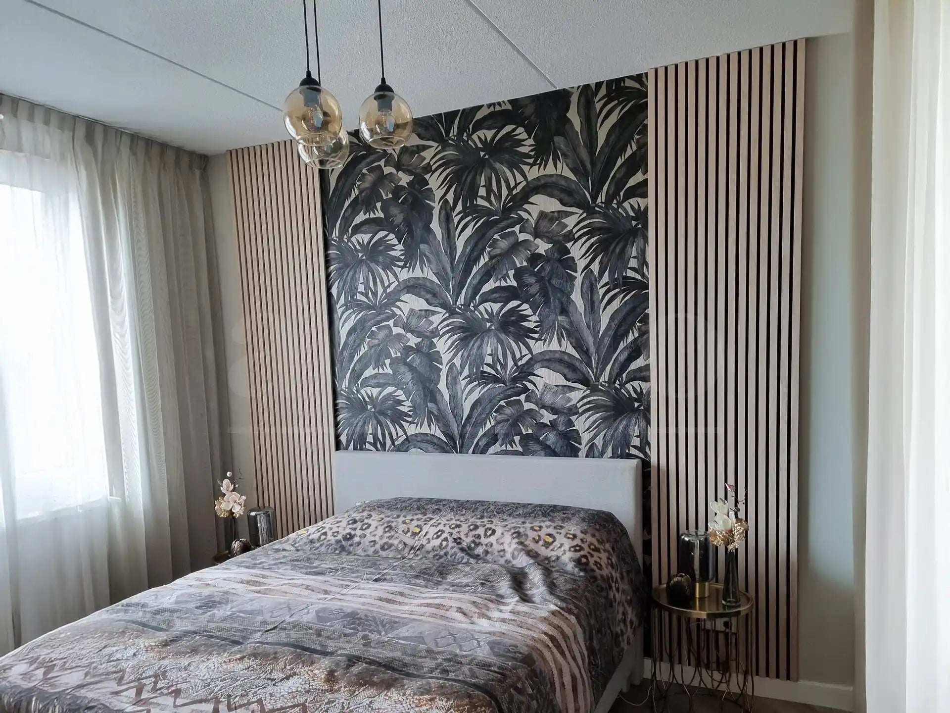 Slaapkamer met Adeqo akoestische panelen in Wit Eiken aan weerszijden van een decoratief zwart-wit bladerenbehang achter het bed.
