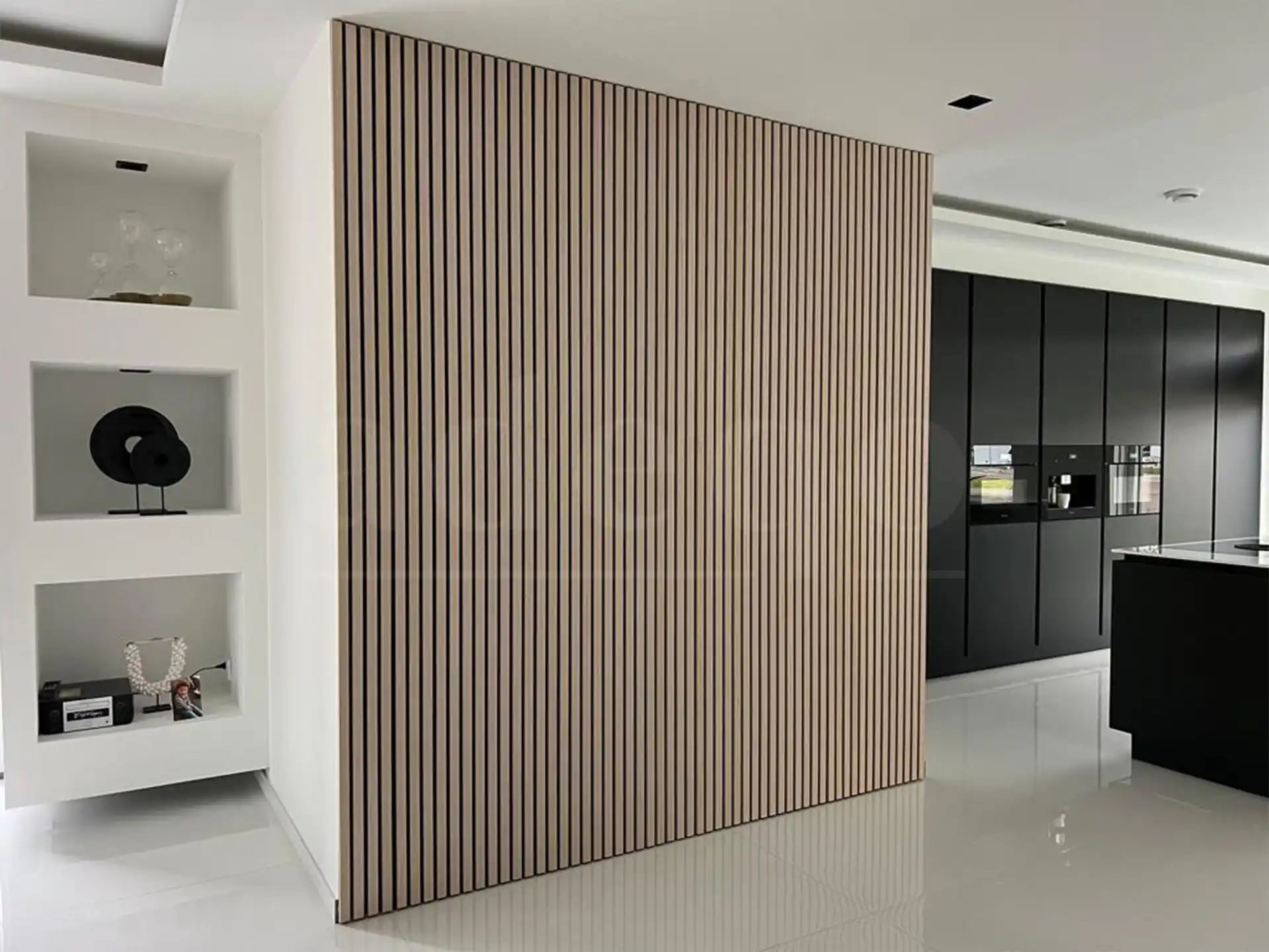 Gesloten verborgen deur bekleed met Adeqo akoestische panelen in Wit Eiken, naadloos geïntegreerd in een moderne witte wand, grenzend aan een zwarte designkeuken.