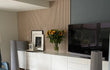 Woonkamer met Adeqo akoestische panelen in Wit Eiken achter een wit dressoir, versierd met zonnebloemen, schilderijen en een televisie.