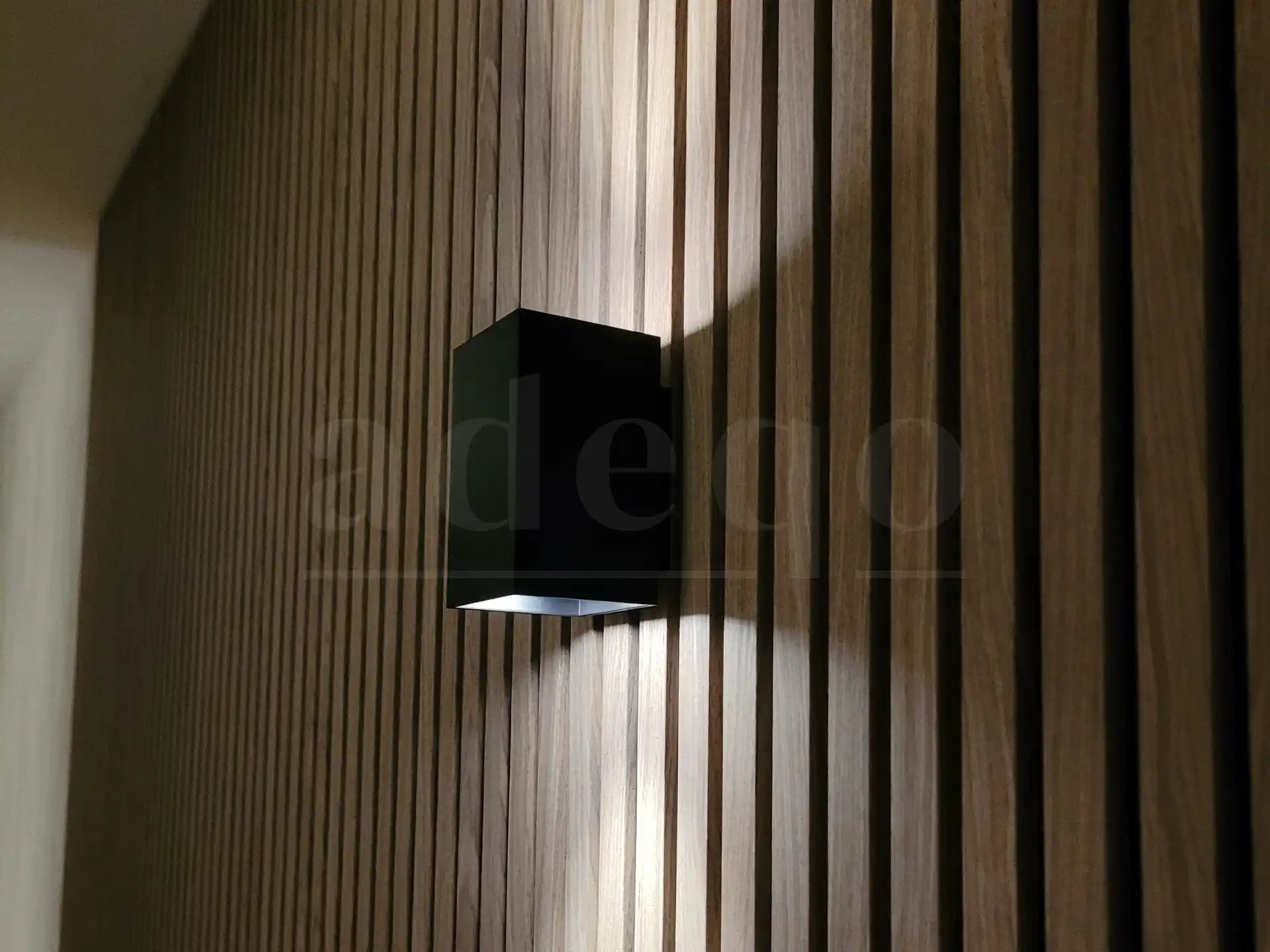 Close-up van Adeqo akoestisch wandpaneel in Licht Walnoot met moderne zwarte wandlamp.