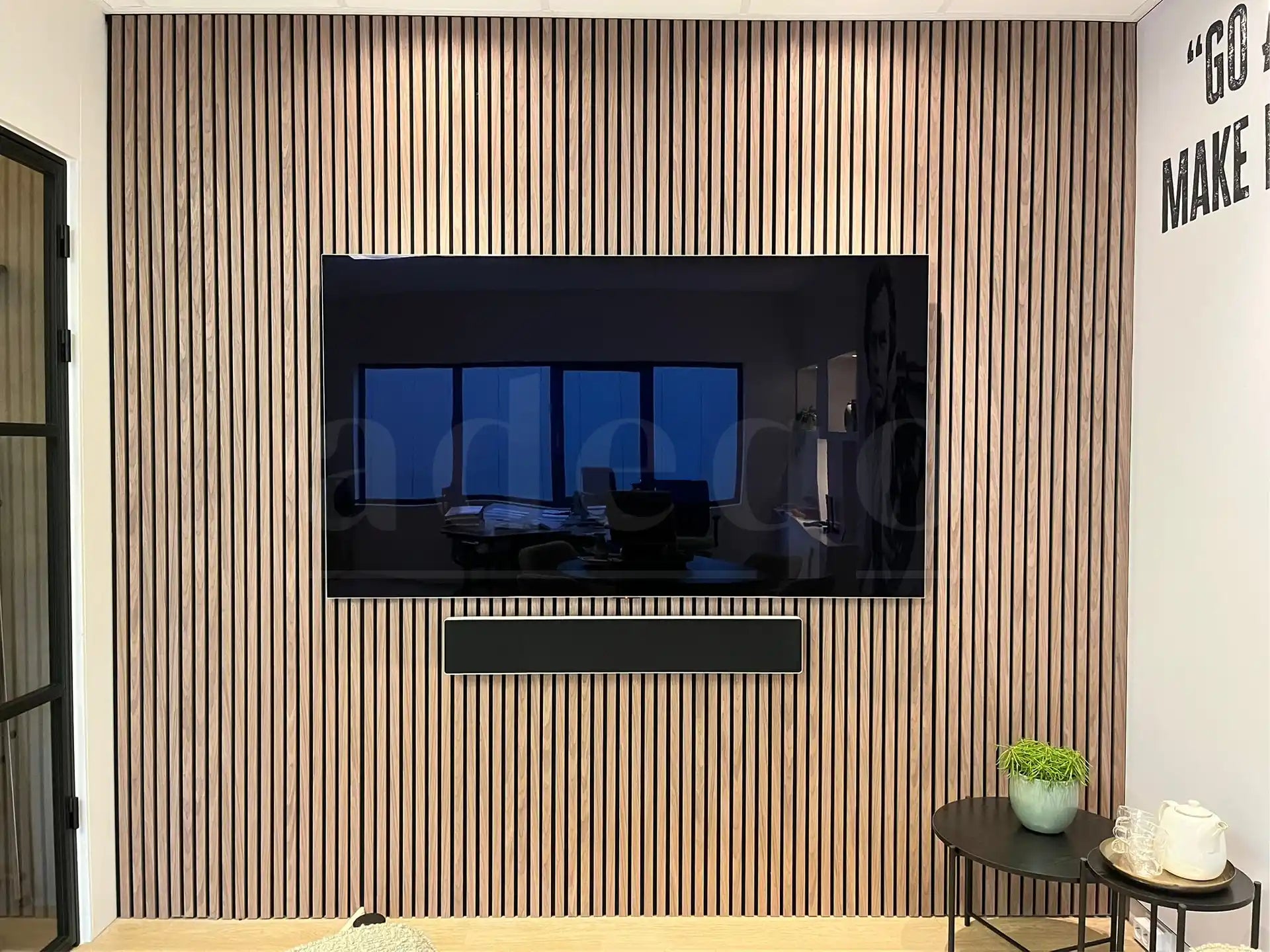 Moderne tv-wand met Adeqo akoestisch wandpaneel in Licht Walnoot, gecombineerd met zwarte en houten accenten.