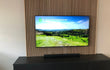 Tv-wand met Adeqo akoestisch wandpaneel in Natuurlijk Eiken achter een zwart tv-meubel.