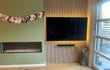 Tv-wand met Adeqo akoestisch wandpaneel in Natuurlijk Eiken en geïntegreerde verlichting, naast groene wand met haard.