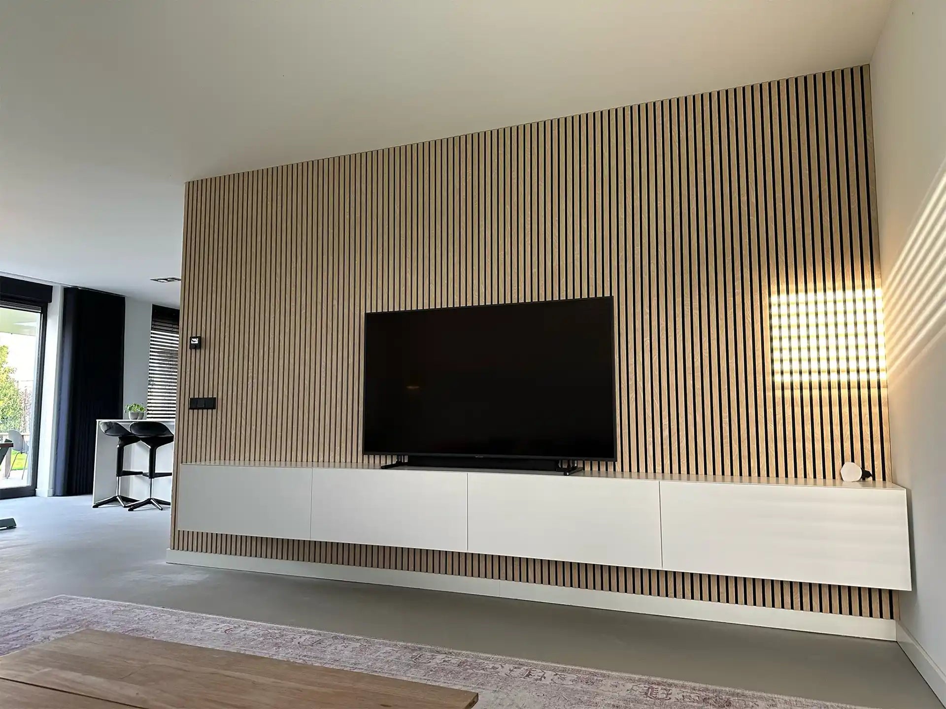 Moderne woonkamer met tv-wand van Adeqo akoestisch wandpaneel in Natuurlijk Eiken en wit zwevend tv-meubel.