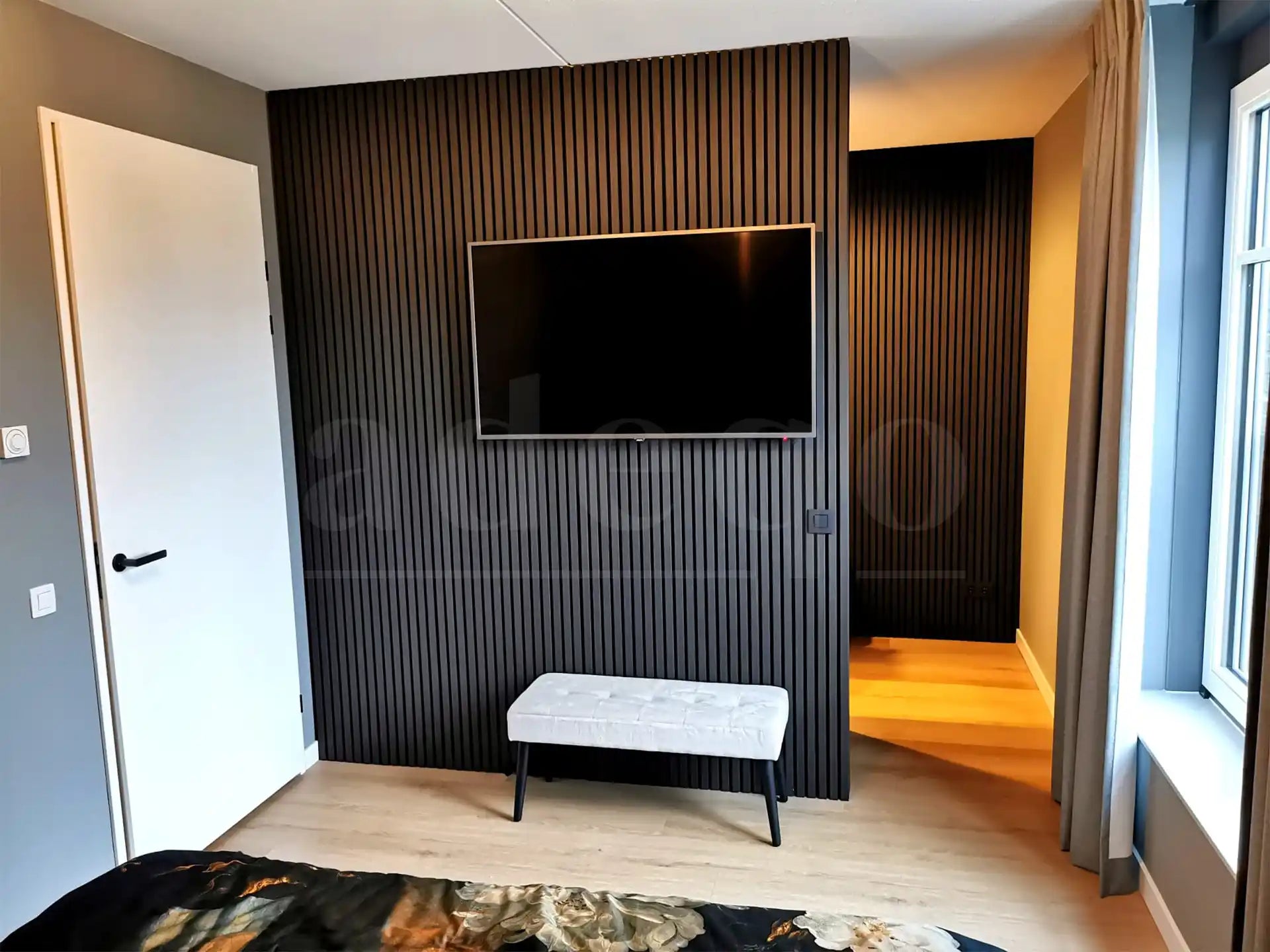 Akoestische wandpanelen in Zwart Eiken als stijlvolle tv-achterwand in een moderne slaapkamer, gecombineerd met een houten vloer en lichte meubels
