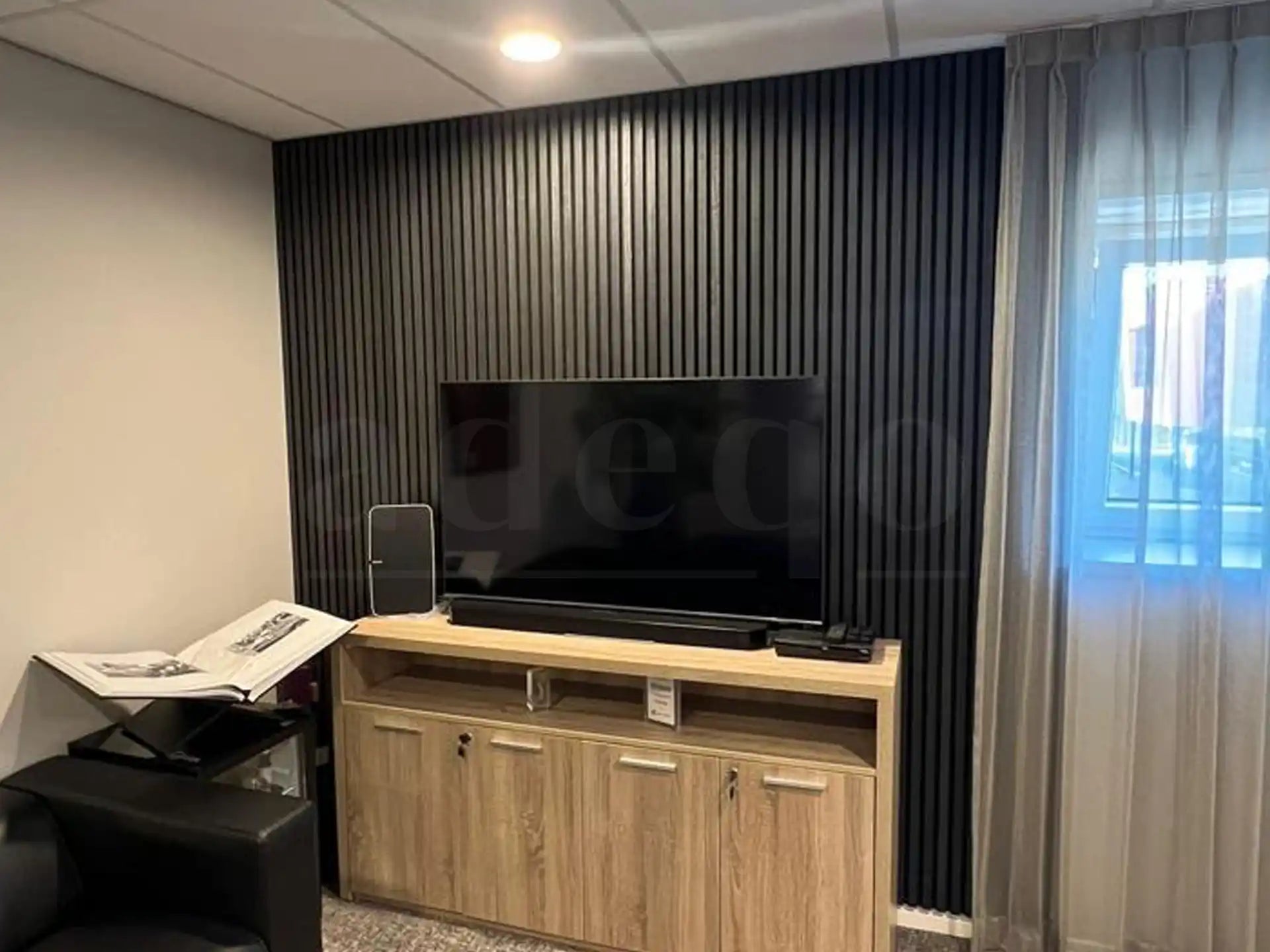 Akoestische wandpanelen in Zwart Eiken als tv-achterwand in een moderne woonkamer, gecombineerd met een houten tv-meubel en neutrale gordijnen.