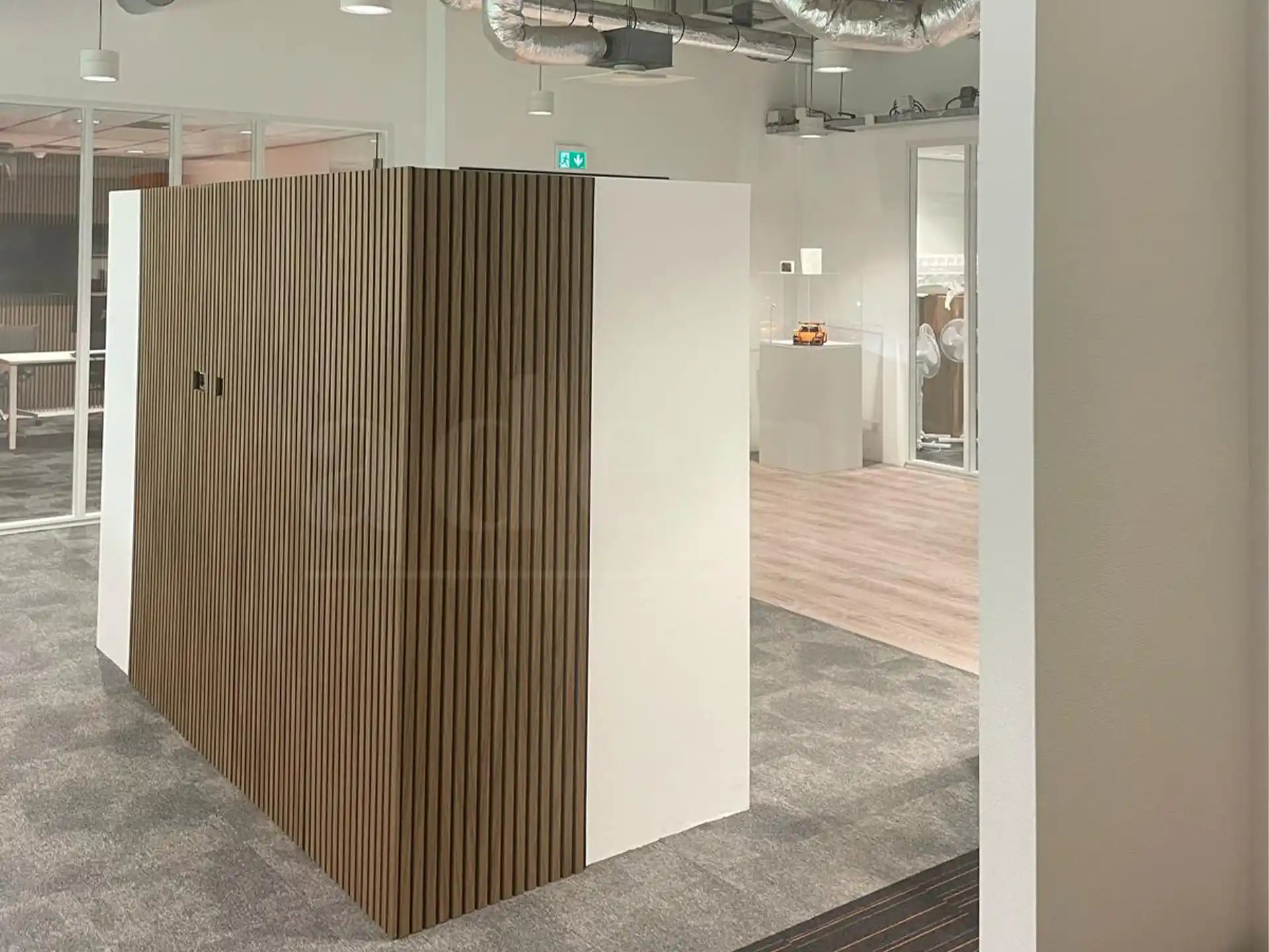 Strakke kantoorwand bekleed met Bruine Eiken akoestische wandpanelen van Adeqo, gecombineerd met witte zijpanelen in een moderne kantooromgeving.