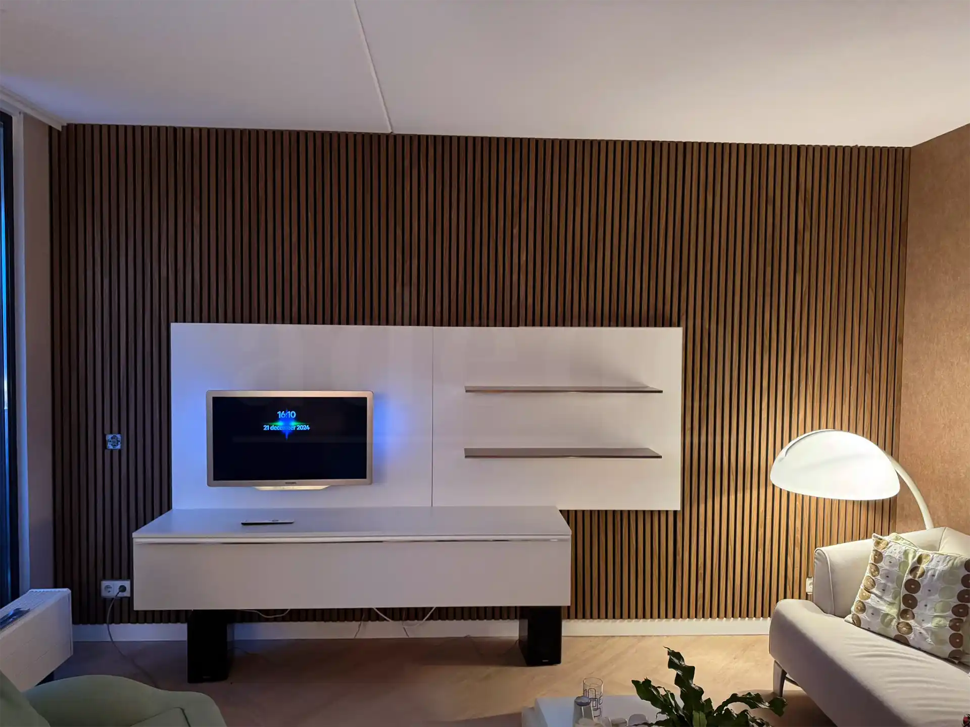Woonkamer met Bruin Eiken akoestische wandpanelen van Adeqo als stijlvolle tv-wand, gecombineerd met wit zwevend meubel en moderne verlichting.