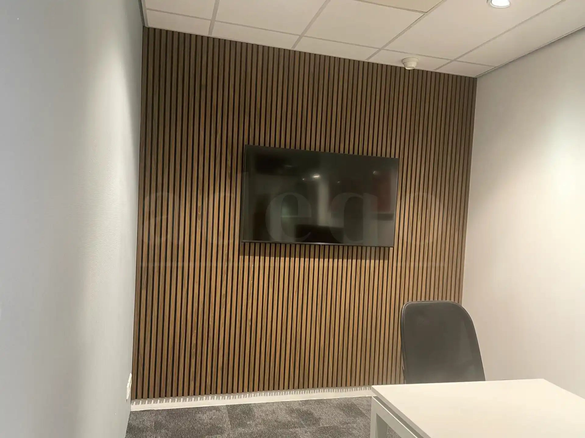Kleine vergaderruimte met Bruine Eiken akoestische wandpanelen van Adeqo, voorzien van een tv-scherm en modern kantoormeubilair.