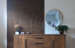 Moderne woonkamer met Adeqo akoestische wandpanelen in Bruin Eiken achter een houten dressoir, gedecoreerd met planten, kaarsen en een ronde spiegel.
