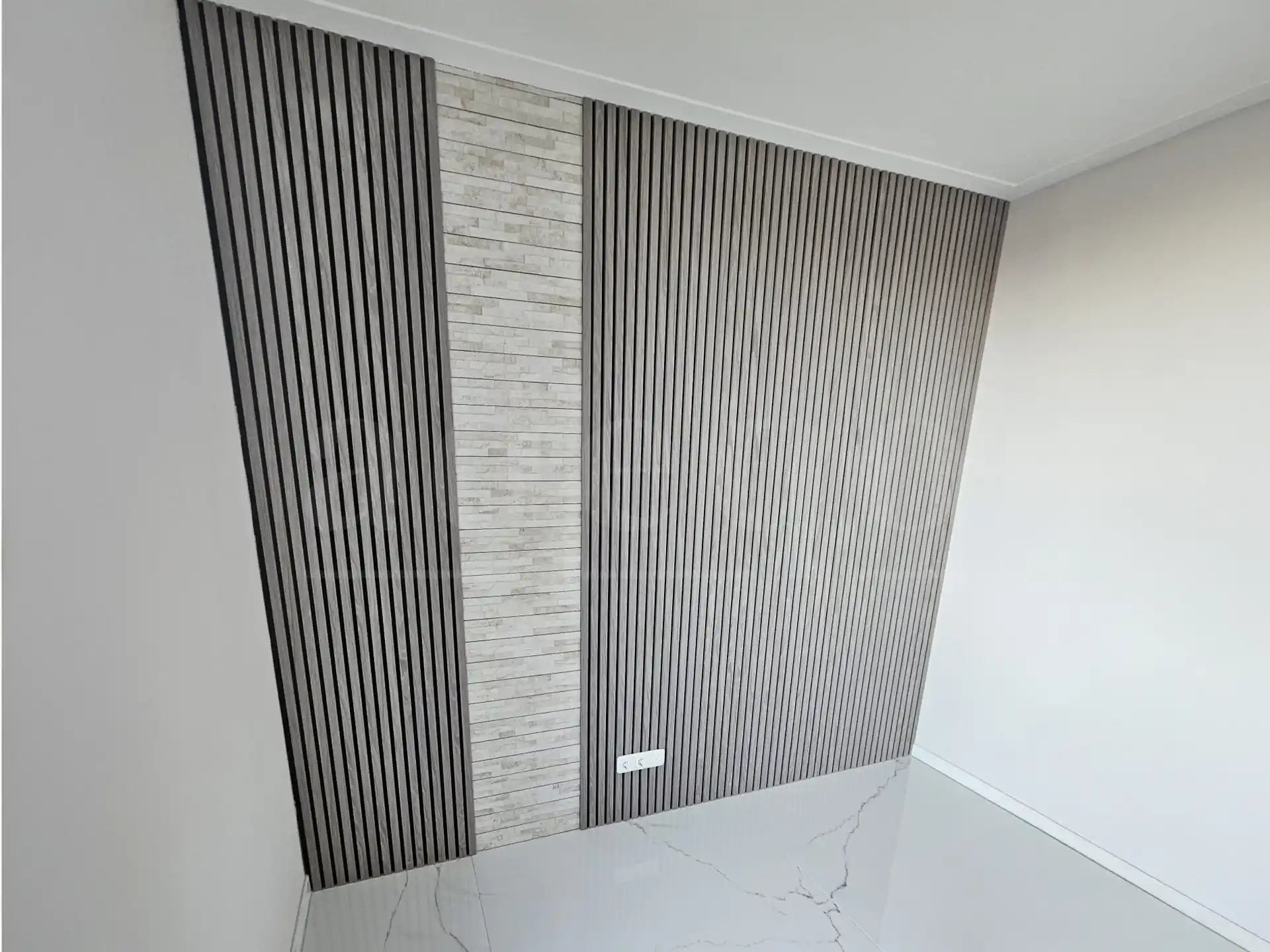 Strakke wandbekleding met Adeqo akoestische wandpanelen in Grijs Eiken, gecombineerd met een middenstrook van licht natuursteen, geplaatst in een moderne ruimte met glanzende witte vloer.