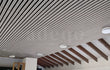 Modern plafond afgewerkt met Adeqo akoestische wandpanelen in Grijs Eiken, voorzien van geïntegreerde ronde inbouwspots en zichtbare houten dakbalken.