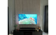 Moderne tv-wand met Adeqo akoestische wandpanelen in Grijs Eiken, gecombineerd met een zwart tv-meubel en sfeervolle verlichting.