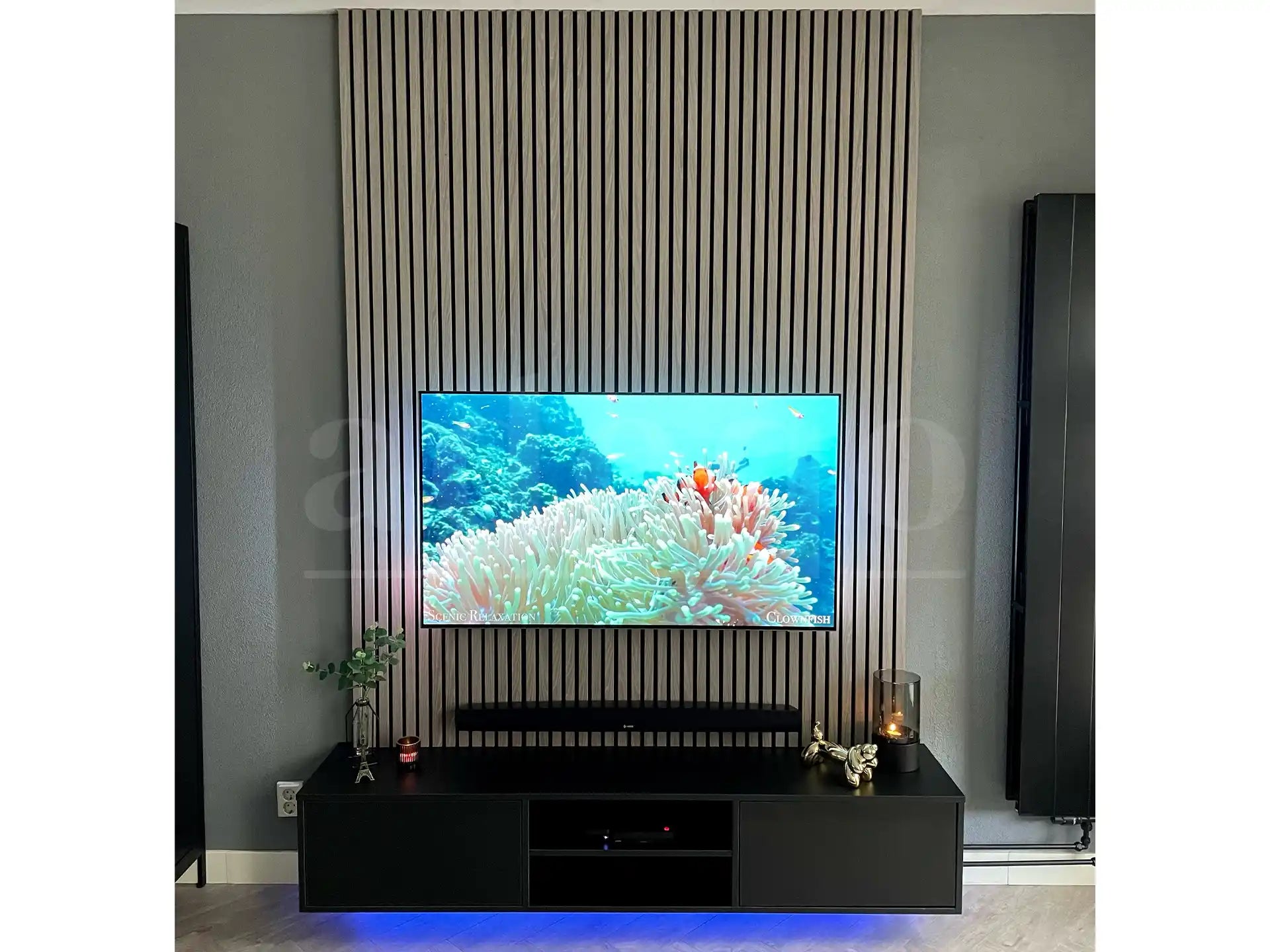 Moderne tv-wand met Adeqo akoestische wandpanelen in Grijs Eiken, gecombineerd met een zwart tv-meubel en sfeervolle verlichting.