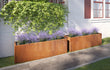 Twee grote cortenstalen plantenbakken van 200x40x80 cm met paarse bloemen naast een moderne woning voor een sfeervolle tuininrichting.