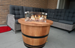 Brandende Adeqo Vuurtafel van eikenhout in ronde vorm met ronde brander, geplaatst op een terras met grijze loungeset.