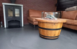 Gezellige Adeqo Vuurtafel van eikenhout in ronde vorm met een ronde brander, geplaatst in een sfeervolle zithoek met haard en bank.