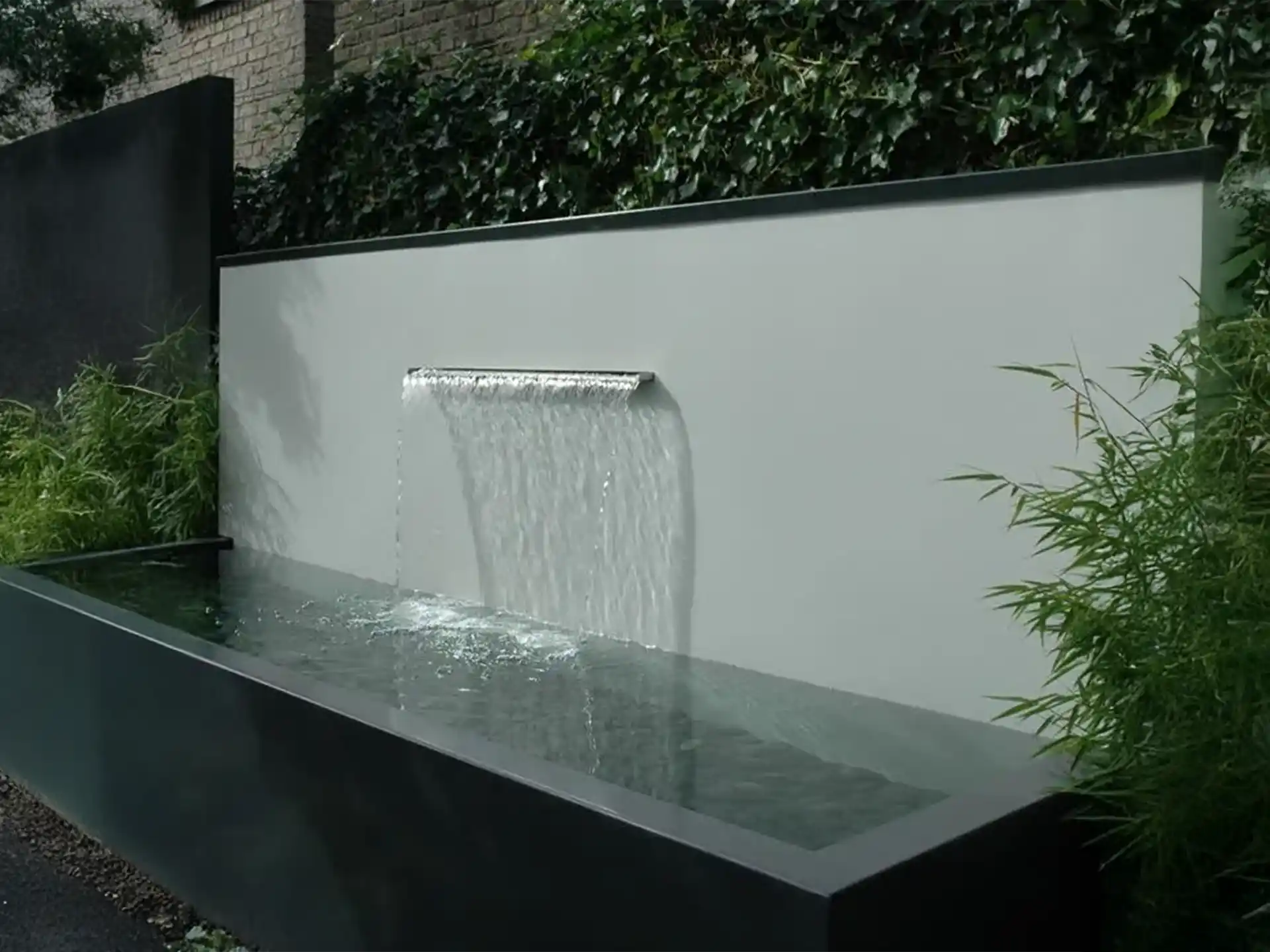 Adezz aluminium vijver met ingebouwde waterval, geplaatst tegen een moderne tuinwand, stromend water voor rustgevende sfeer.