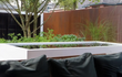 Adezz aluminium vijver in een moderne tuin, gevuld met water en strak afgewerkt, naast een zithoek met kussens.