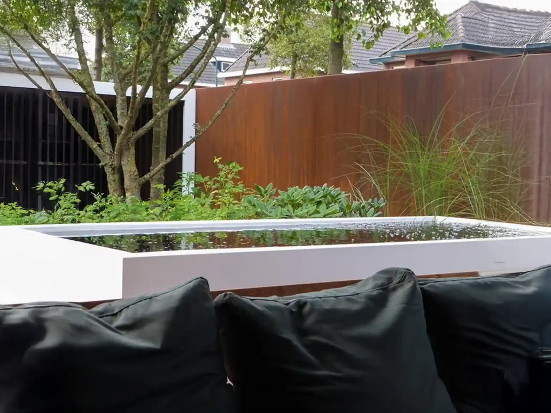 Adezz aluminium vijver in een moderne tuin, gevuld met water en strak afgewerkt, naast een zithoek met kussens.