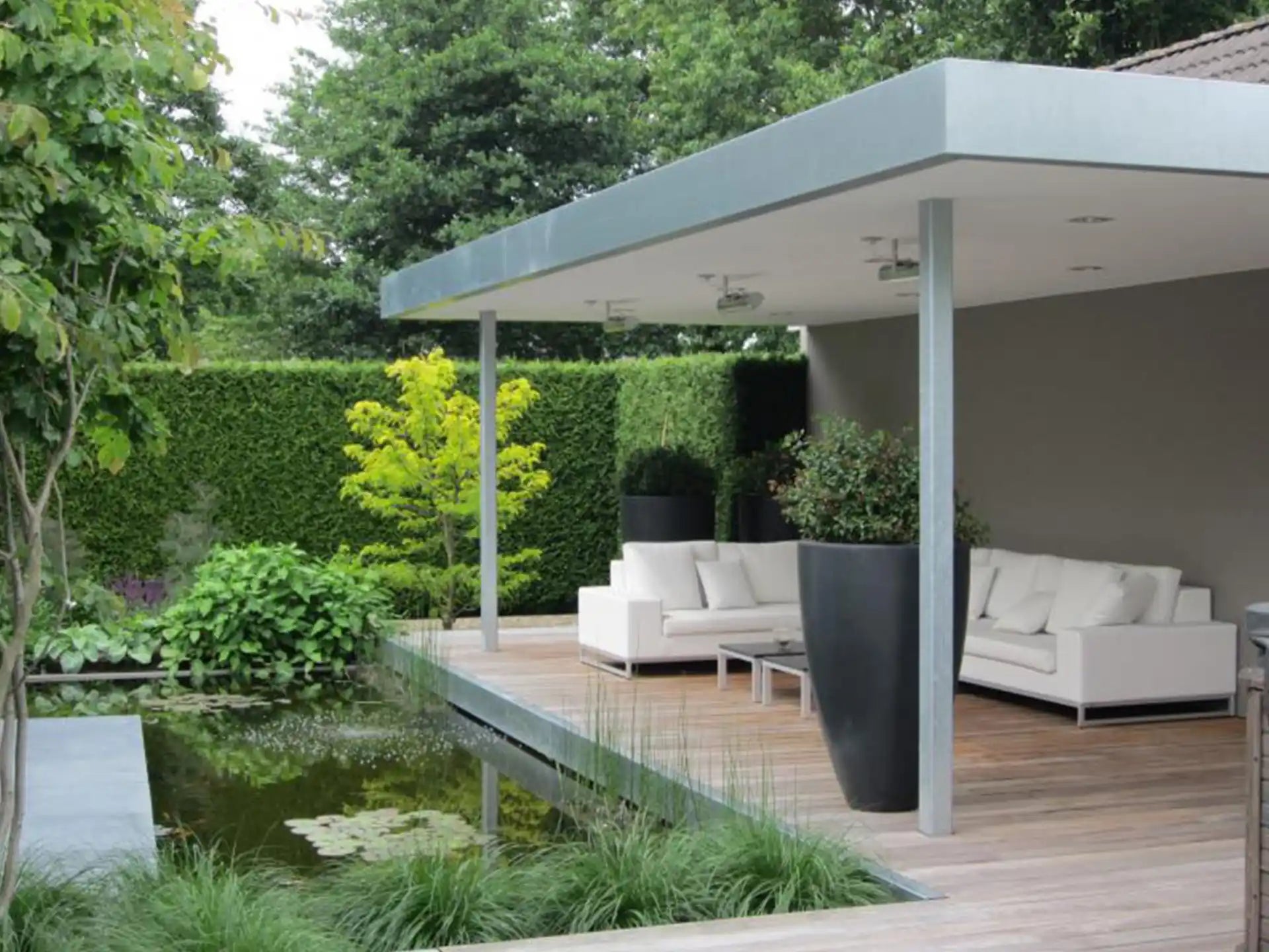 Grote ronde Adezz Canna polyester plantenbak in donkergrijs naast een moderne overkapping met vijver.
