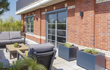 Meerdere rechthoekige Adezz Carrez aluminium plantenbakken met wielen naast een moderne woning en lounge set.