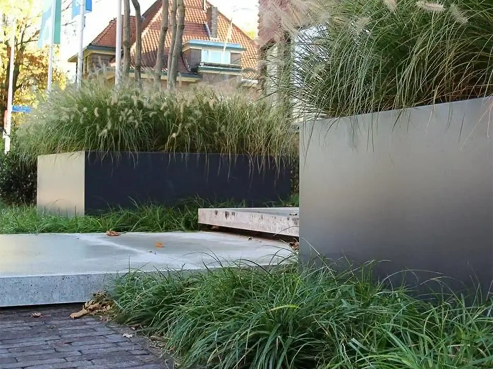 Grote rechthoekige Adezz Carrez aluminium plantenbak zonder bodem langs een straat, gevuld met siergrassen.
