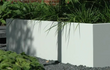 Witte Adezz Carrez aluminium plantenbak zonder bodem in een tuin, beplant met siergrassen en omgeven door grind.