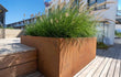 Adezz Carrez Cortenstaal Plantenbak met bodem, gevuld met siergrassen op een modern houten terras.