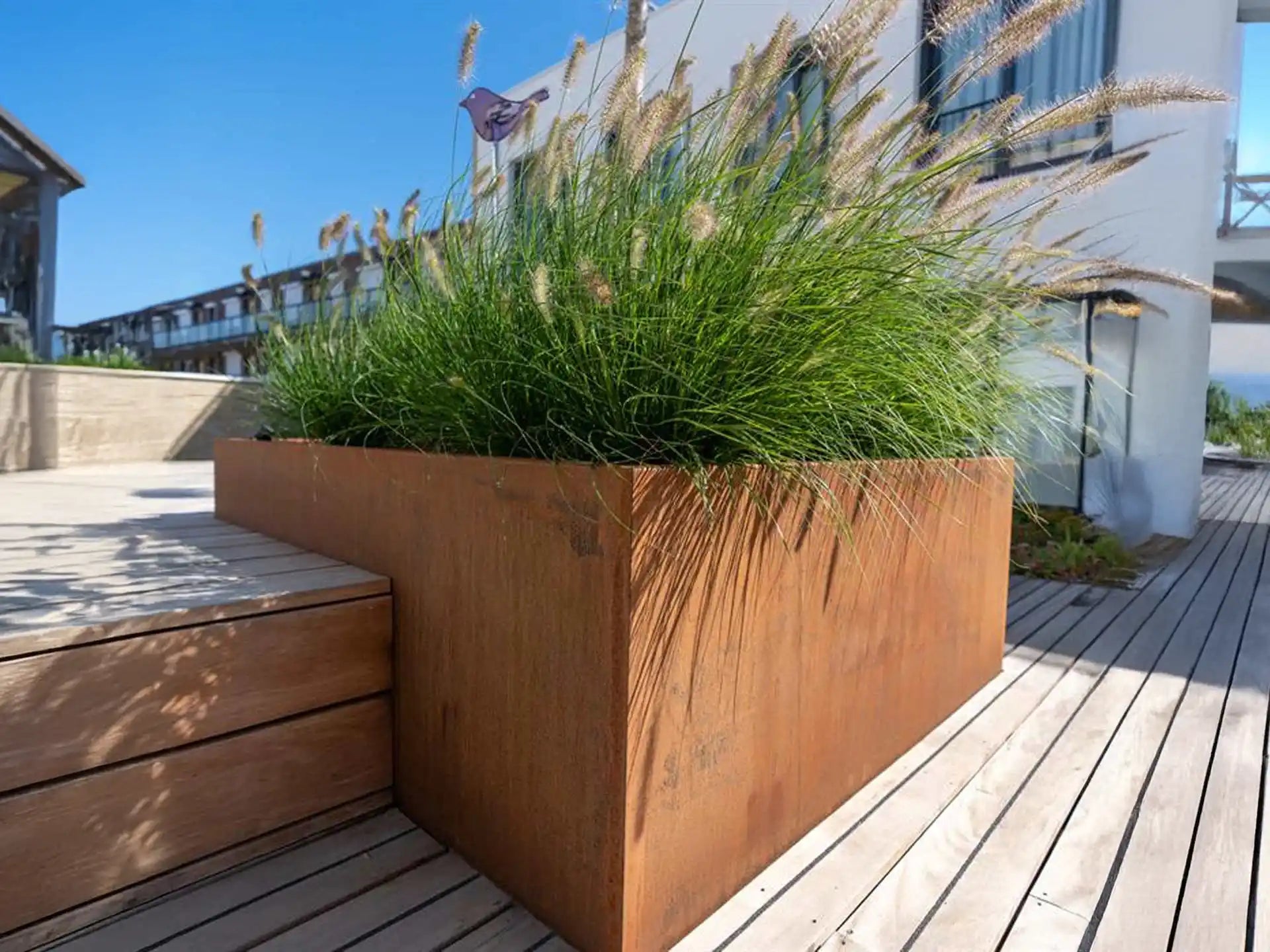 Adezz Carrez Cortenstaal Plantenbak met bodem, gevuld met siergrassen op een modern houten terras.