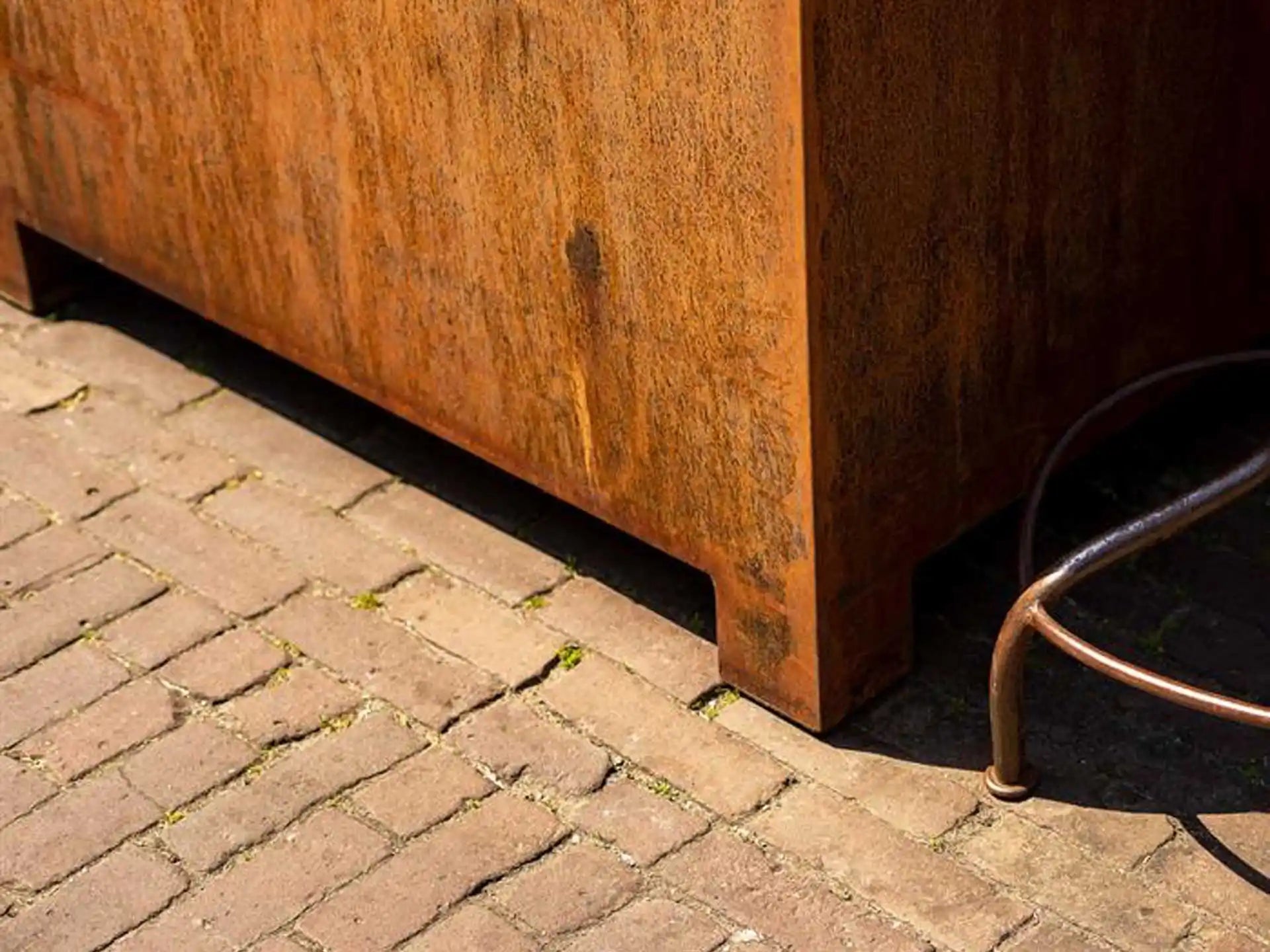 Close-up van de Adezz Carrez Cortenstaal Plantenbak Rechthoek met poten en bodem, geplaatst op een straat met klinkers.