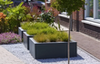 Adezz Carrez polyester plantenbak in antraciet, geplaatst naast een oprit met groene beplanting.