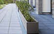 Taupe kleurige Adezz Carrez polyester plantenbak met wielen, geplaatst langs een moderne gevel met beplanting.