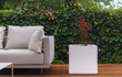 Strakke witte Adezz Carrez polyester plantenbak naast een loungehoek op een houten terras.