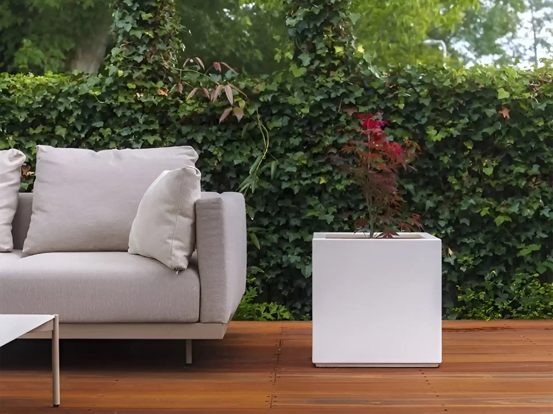 Strakke witte Adezz Carrez polyester plantenbak naast een loungehoek op een houten terras.