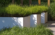 Witte Adezz Carrez polyester plantenbak met siergras, toegepast op een terras met houten pergola.