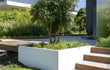 Witte Adezz Carrez polyester plantenbak met siergrassen en bomen in een moderne tuin.
