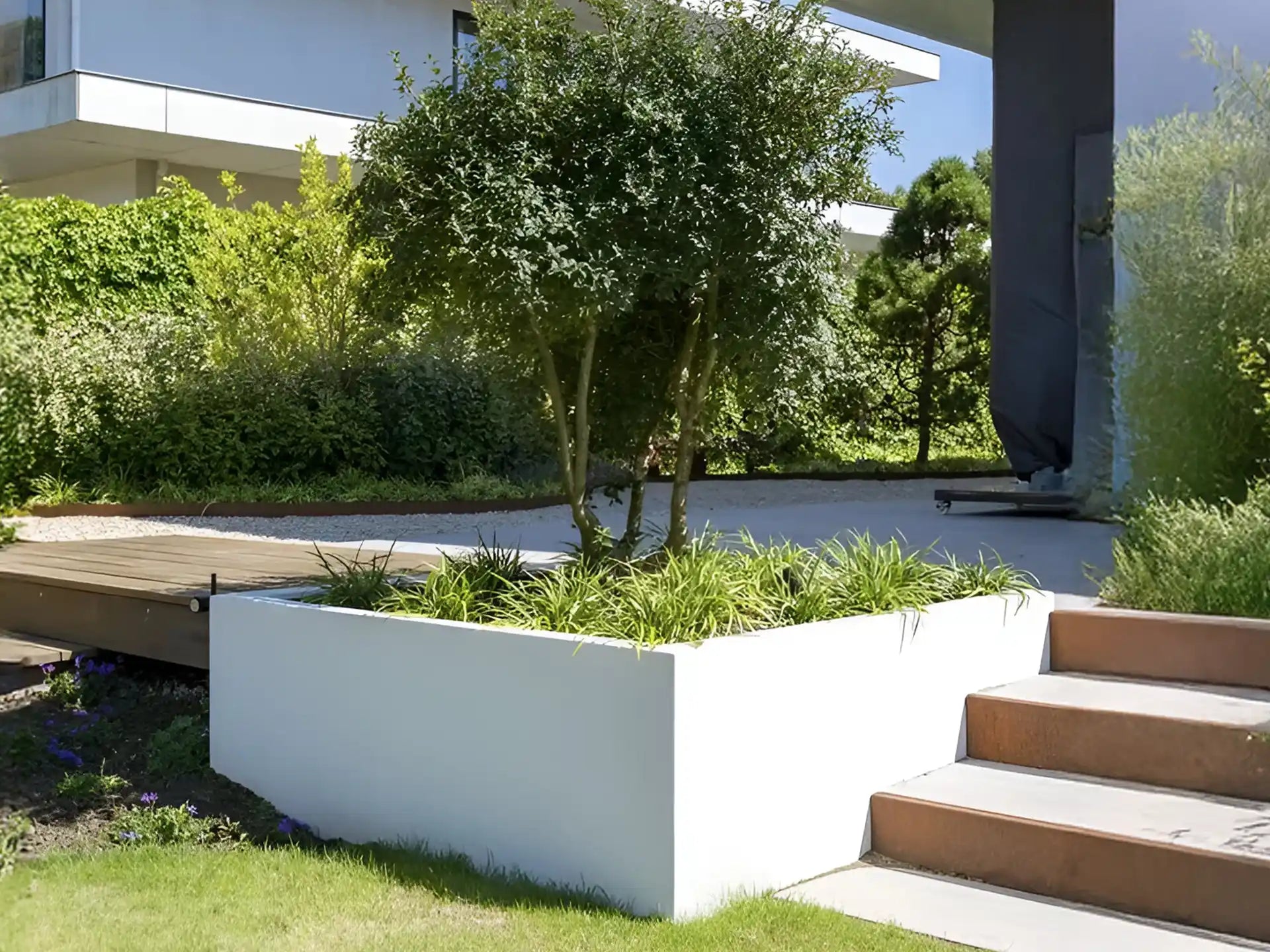 Witte Adezz Carrez polyester plantenbak met siergrassen en bomen in een moderne tuin.