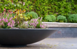  Adezz Ceder polyester plantenbak rond schaalmodel met kleurrijke bloemen in een tuinomgeving.