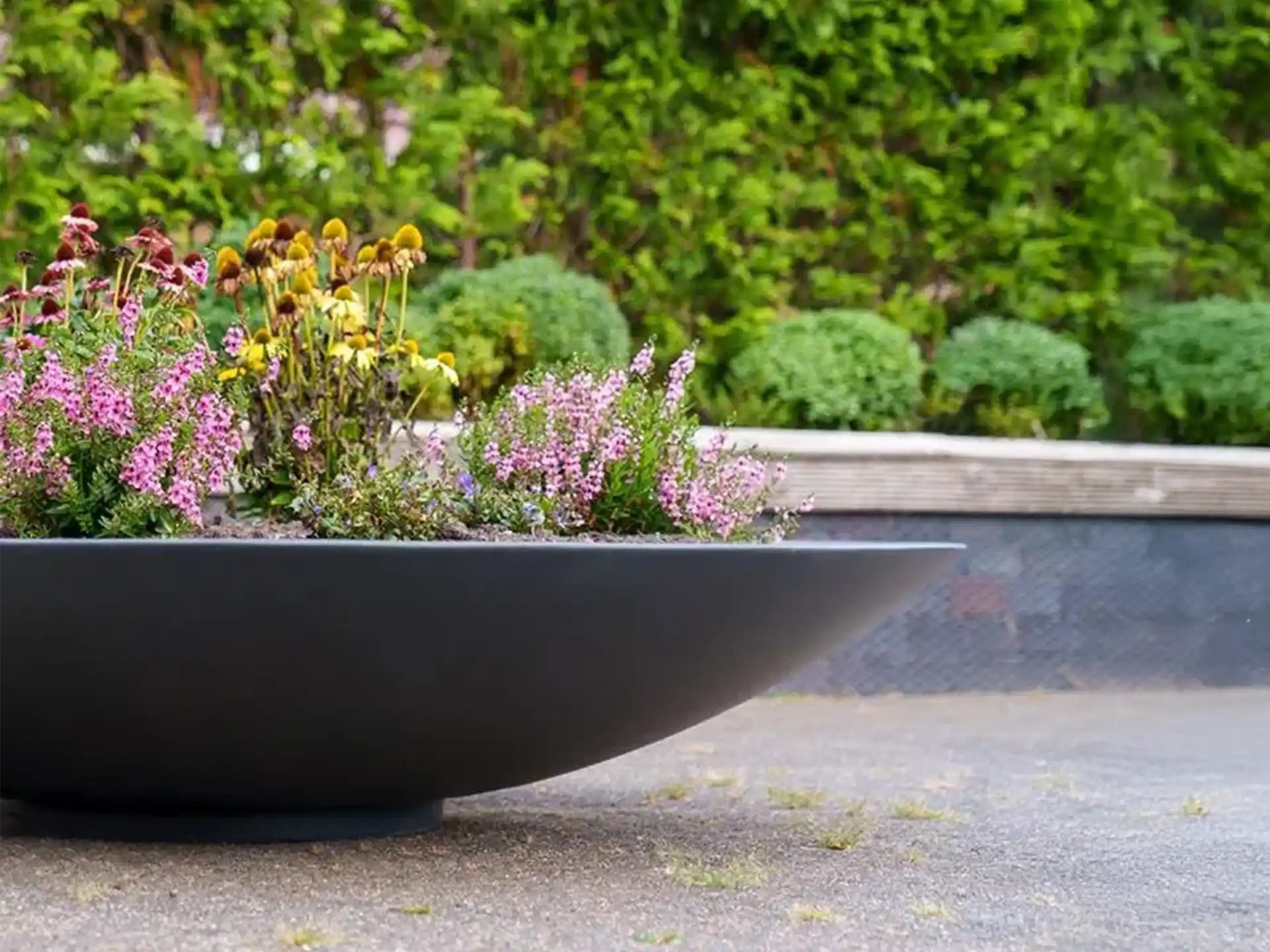  Adezz Ceder polyester plantenbak rond schaalmodel met kleurrijke bloemen in een tuinomgeving.