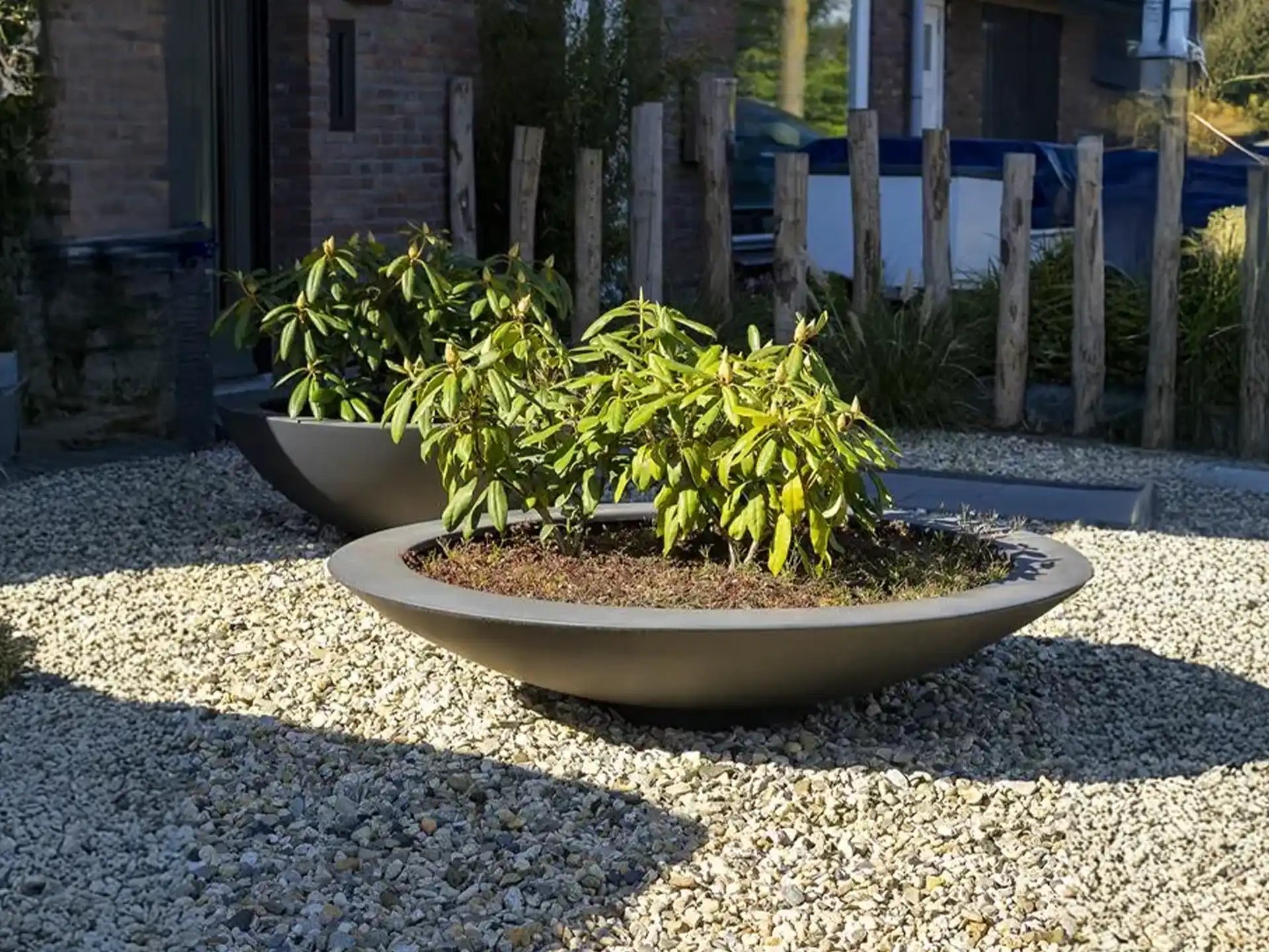 Twee Adezz Ceder polyester plantenbakken rond schaalmodel gevuld met sierplanten op grind.
