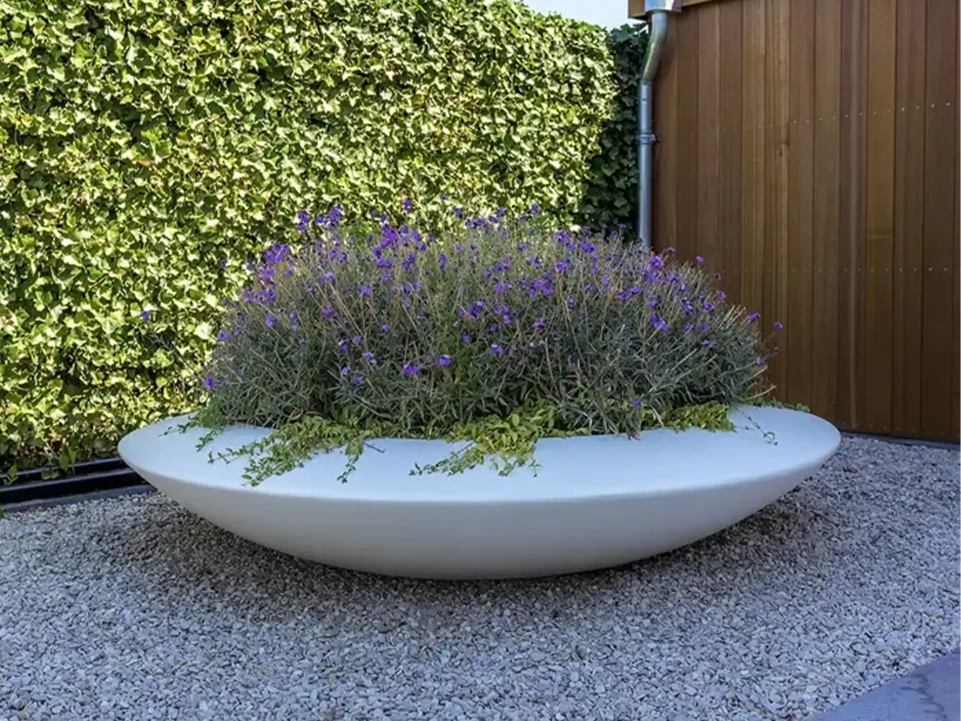 Adezz Ceder polyester plantenbak rond schaalmodel in wit met paarse bloemen, geplaatst op grind.