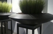 Adezz Ceder polyester plantenbak rond schaalmodel in zwart met hoge grassen, geplaatst in een moderne setting.