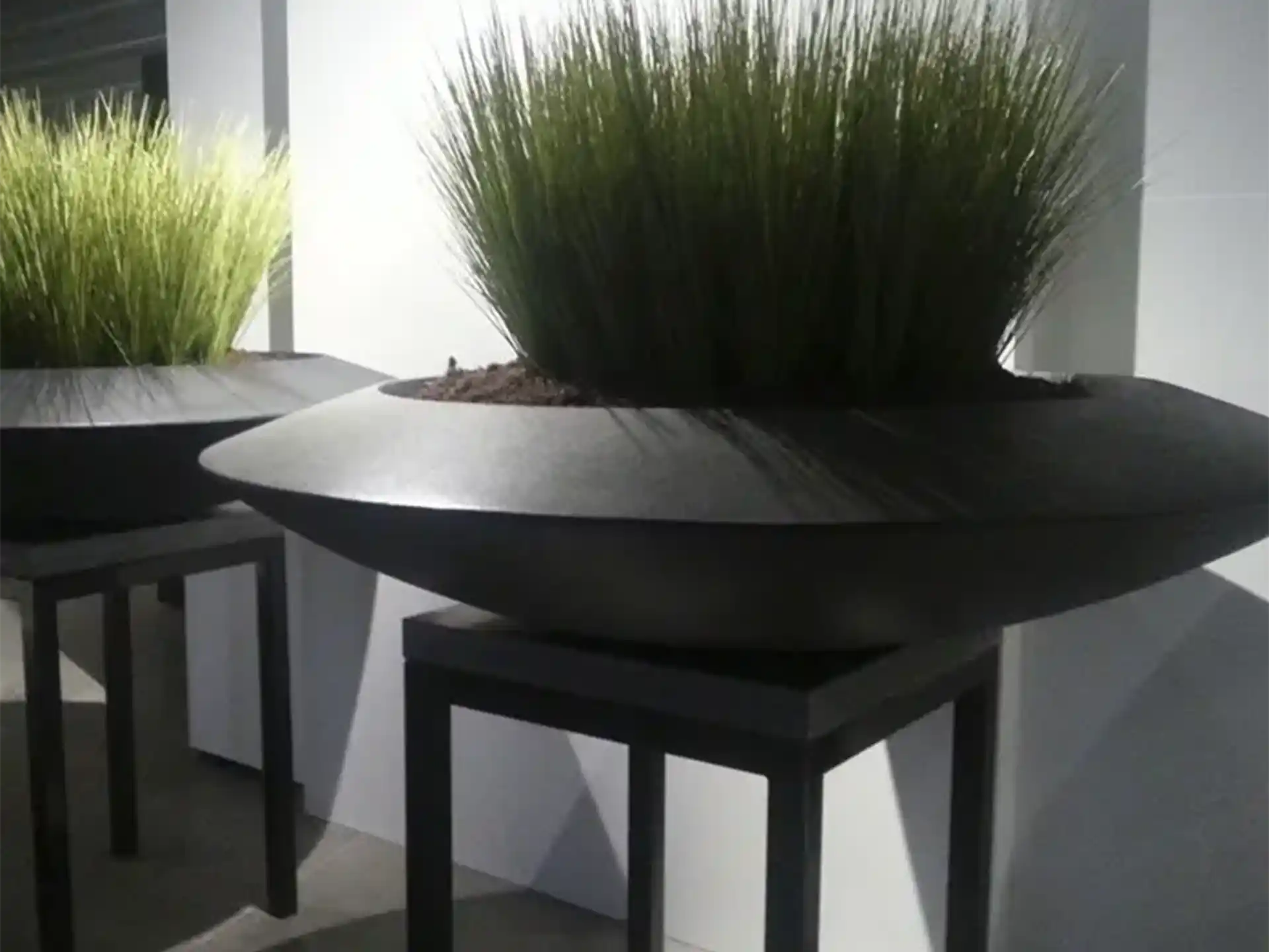 Adezz Ceder polyester plantenbak rond schaalmodel in zwart met hoge grassen, geplaatst in een moderne setting.
