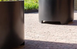 Zwarte Adezz Circum aluminium plantenbak met moderne poten op een terras met bestrating.