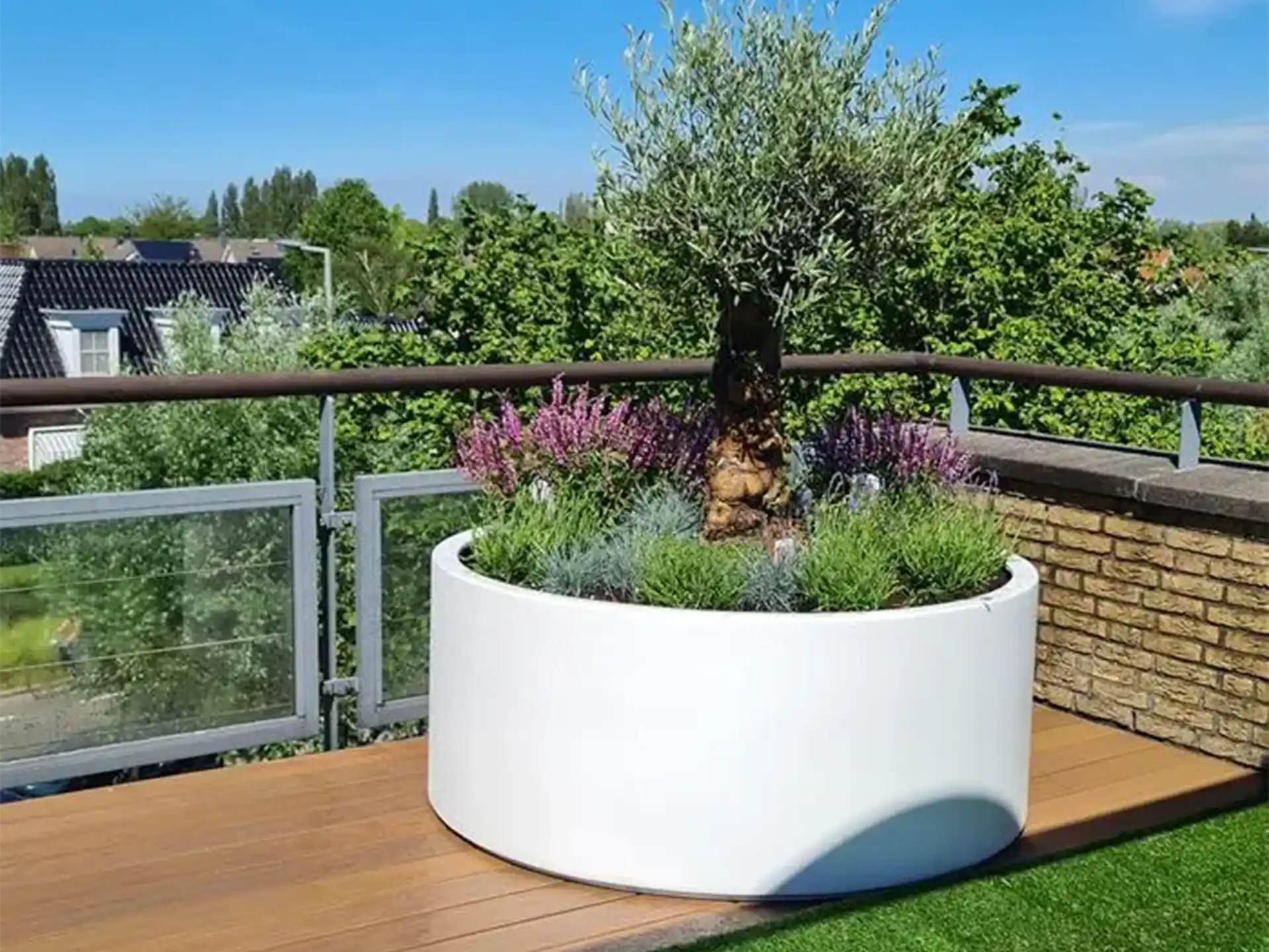 Witte Adezz Circum aluminium plantenbak rond met olijfboom en kleurrijke beplanting op een dakterras.